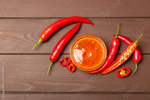 Foto Hot chili sauce  in a bowl with fresh red peppers and chili flakes on wooden cutting board