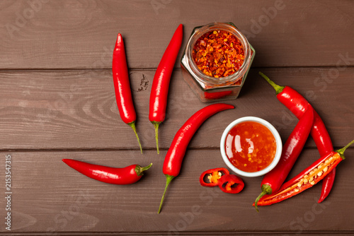 Foto Hot chili sauce  in a bowl with fresh red peppers and chili flakes on wooden cutting board