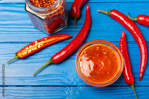 Fotografie Hot chili sauce  in a bowl with fresh red peppers and chili flakes on wooden cutting board