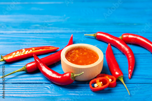 Obraz na płótnie Hot chili sauce  in a bowl with fresh red peppers and chili flakes on wooden cutting board
