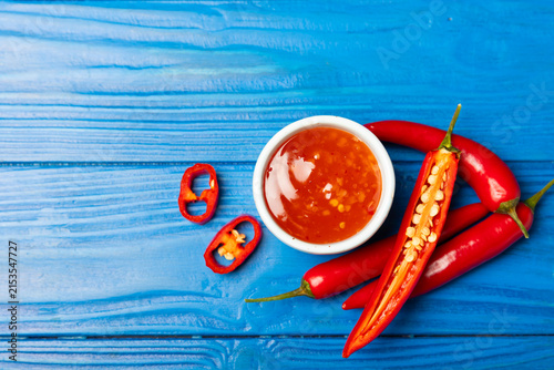Konstfotografi Hot chili sauce  in a bowl with fresh red peppers and chili flakes on wooden cutting board