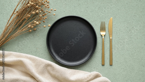 Minimalist table setting with black plate, gold cutlery and dried flowers