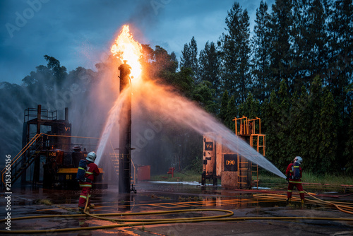 Firefighter Team Fighting a Large Industrial Fire with Powerful Water Streams and Hoses across a Wet Emergency Response Site