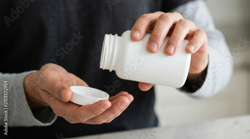 White bottle supplement pill capsule hand male adult medicine healthcare closeup pouring pill from white bottle into male hand for daily supplement and treatment concept