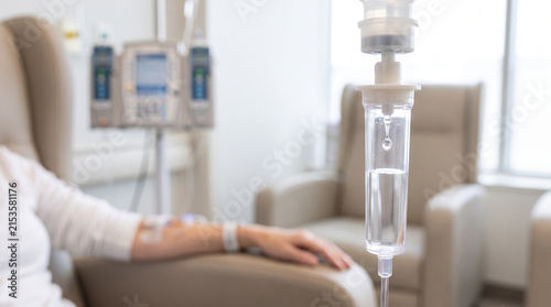 Patient receiving IV infusion in clinic chair with drip stands in background, showing chemotherapy treatment