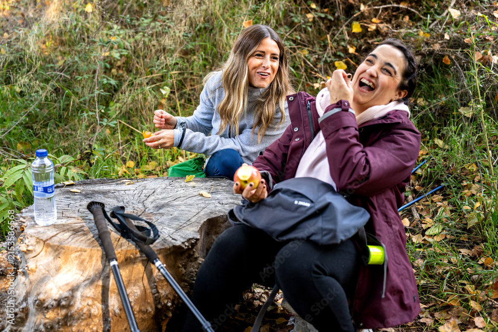 Obraz premium Friends laughing and relaxing during autumn nordic walking break, enjoying healthy snack