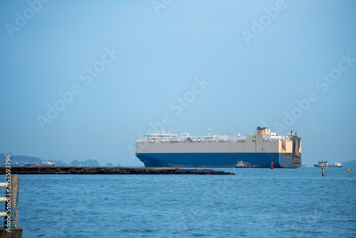 Large car carrier ship navigating calm coastal waters on clear day