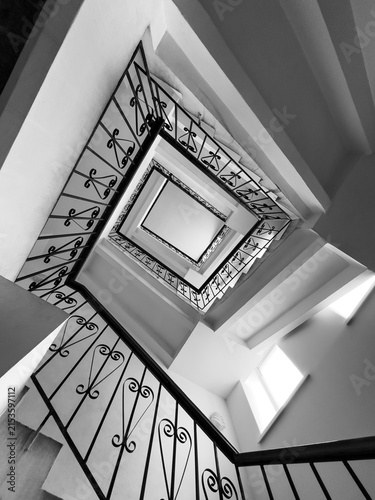 Black and white bottom up view of square spiral staircase with wrought iron railing