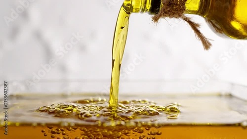 Golden olive oil pouring from glass bottle into clear container with bubbly splash