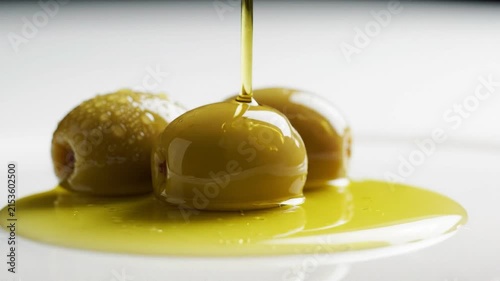 Golden olive oil pouring over fresh green olives on a clean white surface