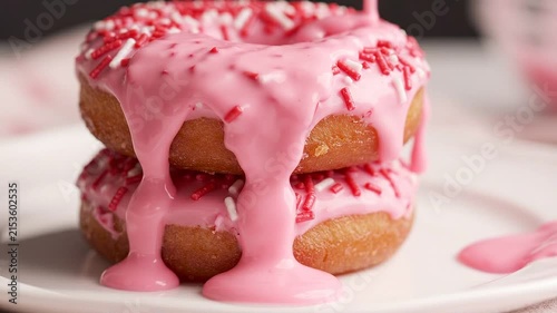 Two pink frosted donuts with drizzled icing and colorful sprinkles on a plate