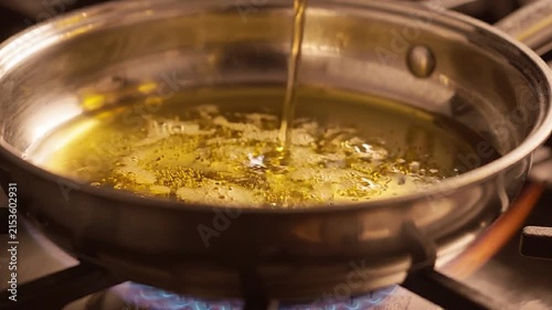 Close-up of golden cooking oil being poured into a stainless steel saucepan on a gas stove
