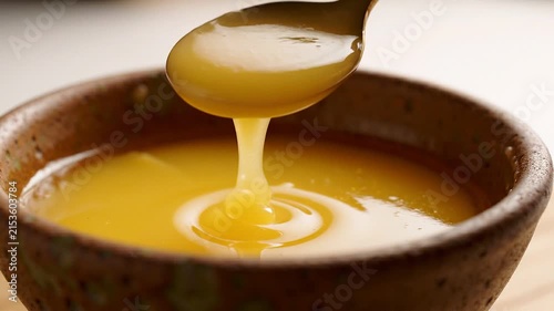 Wooden spoon dipping into a bowl of golden clarified butter ghee for cooking