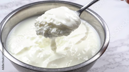 Close-up of a spoon scooping creamy white yogurt from a metal bowl on marble