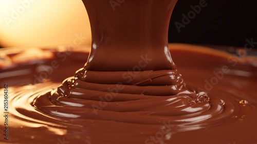 Thick, velvety melted chocolate pouring in rich, glossy swirls on a warm surface