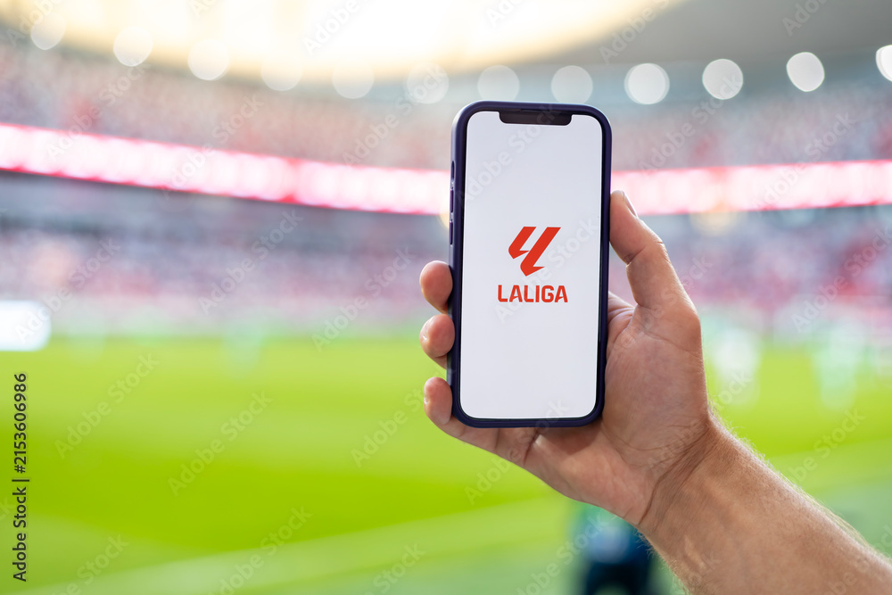 Fototapeta premium MINSK, BELARUS JUNE 9, 2026: Man holding Apple iPhone 12 in the stadium. The official logo of the Spanish championship in football, La Liga. Liga de Futbol Profesional, LFP