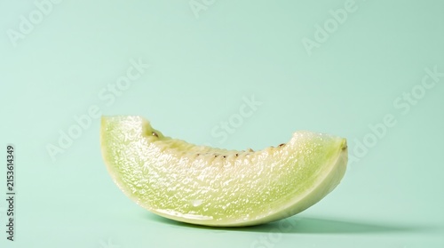 Sliced honeydew melon rests against a pale green background