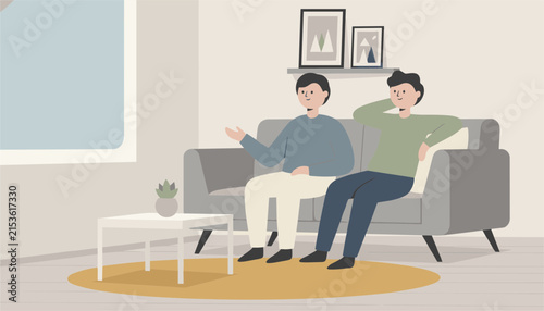 Two men having a relaxed conversation while sitting on a grey sofa in a minimalist living room with artwork on the wall.