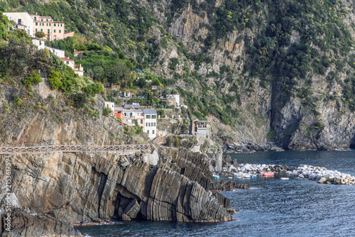 Manarola in coastal Liguria, Italy features striated rock arch below hillside buildings in clear to lightly cloudy weather.