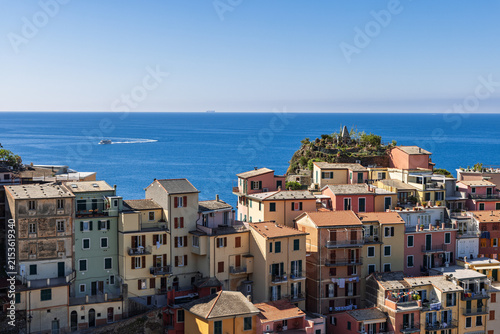 Manarola in Italy inside the Cinque Terre national park features colorful upper village facades and balconies with a clear sky overhead.