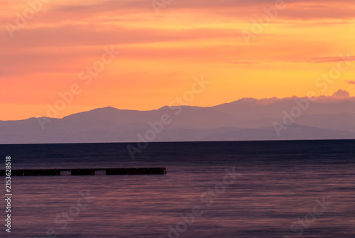 Tramonto arancione sul mare con montagne all'orizzonte