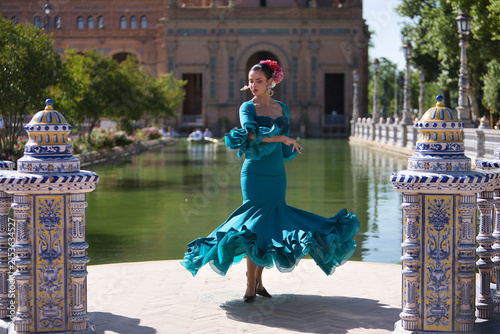 Young, brunette, Andalusian woman, beautiful, wearing a green flamenco dress and flowers in her hair, dancing flamenco, with the canal in the background, in Spain Square in Seville.