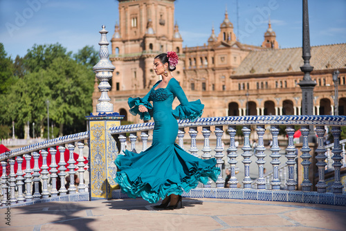 Young, brunette, Andalusian woman, beautiful, wearing a green flamenco dress and flowers in her hair, dancing flamenco on a pretty bridge in Spain Square in Seville.