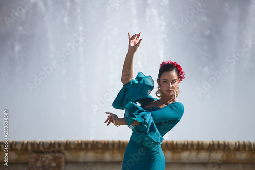 Young, brunette, Andalusian woman, beautiful, wearing a green flamenco dress and flowers in her hair, dancing flamenco, with a beautiful fountain behind her, in Spain Square in Seville.