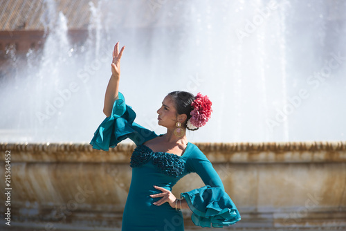 Young, brunette, Andalusian woman, beautiful, wearing a green flamenco dress and flowers in her hair, dancing flamenco, with a beautiful fountain behind her, in Spain Square in Seville.