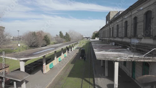 High angle view from the pedestrian bridge showing covered platforms, historic building, and tracks at La Plata El Provincial station, Argentina. D-Log M, 10-bit color, flat log profile.