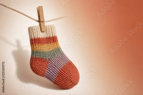 Handmade baby sock hanging on clothesline with pastel knitted stripes