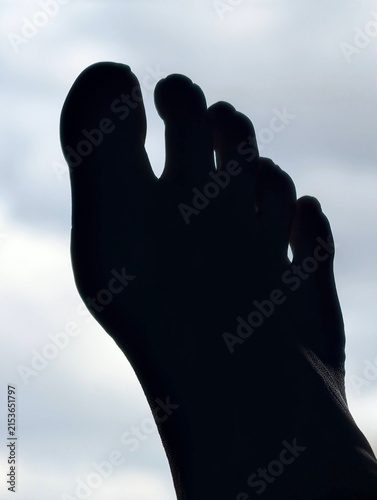 Konstfotografi A dark shadow of a foot pointed up at a cloudy sky