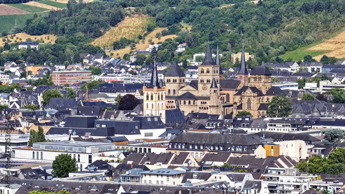 Malerische Stadtansicht von Trier mit dem monumentalen Dom und der Liebfrauenkirche inmitten von Wohnhäusern vor den bewaldeten Hügeln und Weinbergen des Moseltals.