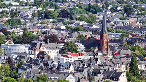 Vogelperspektive auf Trier mit dem markanten Turm der Herz-Jesu-Kirche, umgeben von einer dichten Struktur aus Wohnhäusern, historischen Fassaden und grünen Bäumen.