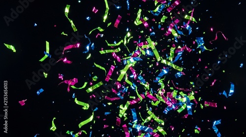 Colorful metallic confetti strips burst against black background for celebration concepts.