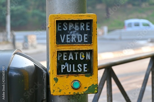 A close-up shot of a typical yellow pedestrian traffic light button in Madrid, Spain. The sign reads 