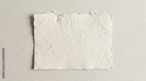 A single piece of textured white handmade paper with rough torn edges isolated on a light beige background for creative projects