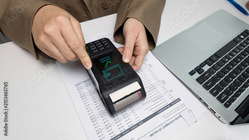 Photography Person using pos terminal for successful payment transaction over income statement document on office desk