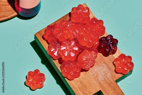 Flower shaped gummy vitamins scattered on a wooden board with a glossy sheen and sharp shadows for health and wellness marketing