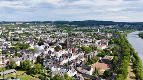 Luftbild von Trier mit der antiken Römerbrücke über die Mosel, umgeben von Stadtarchitektur und grünen Hügeln unter bewölktem Himmel an einem Sommertag.