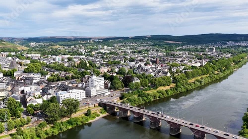 Luftbild von Trier mit der antiken Römerbrücke über die Mosel, umgeben von Stadtarchitektur und grünen Hügeln unter bewölktem Himmel an einem Sommertag.
