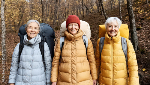 Three senior women hikers with backpacks smile cheerfully in an autumn forest