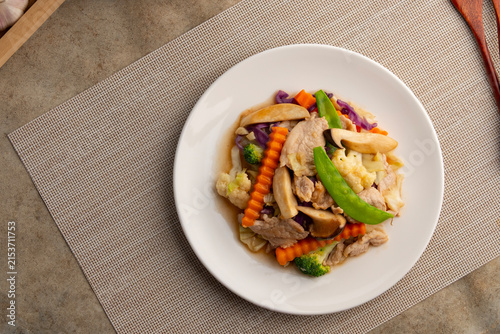stir-fried vegetables with pork and mushroom (Pad Phak Ruam Mid).sliced pork with carrot ,cauliflower ,broccoli ,cabbage ,red cabbage ,Sugar Pea and King Oyster Mushroom in white plate.Top view.