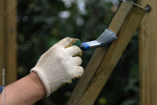 A man's hand in a construction glove uses a paintbrush to impregnate a wooden beam with an antiseptic compound. Protecting wood from biological degradation.