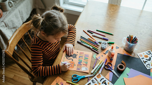 Girl doing arts and crafts at wooden table with colorful markers and paper, top view of creative child engaged in coloring activity at home