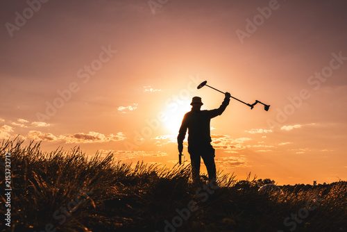 Silhouette of a Detectorist Lifting His Tool Skyward at Golden Hour