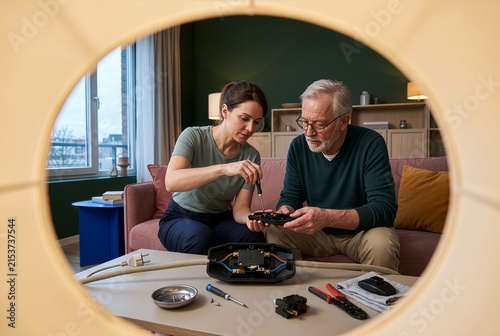 Repair technician and older homeowner fixing an unplugged floor lamp foot switch at home, illustrating household repair, skill sharing, product longevity and sustainable consumption.