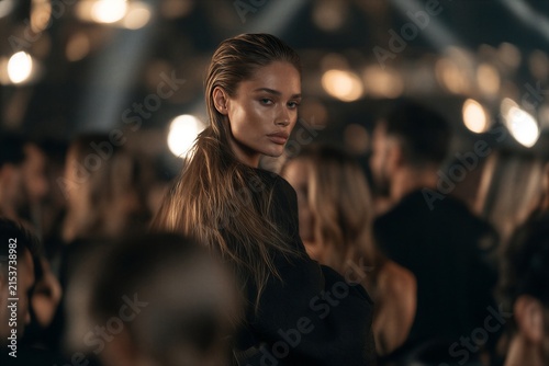 Elegant Young Woman in Black Dress at Crowded Fashion Event