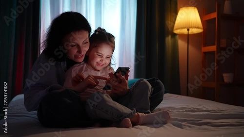 A joyful mother and a small child use smart phones in the evening,time together