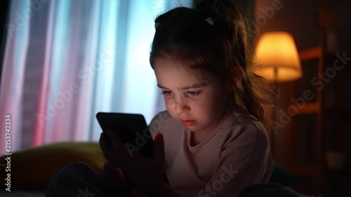 The face of a child using a smartphone in a dark room
